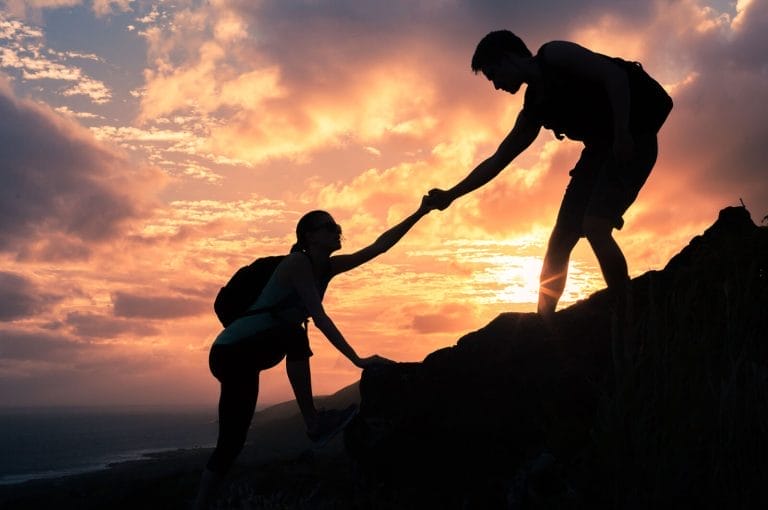 Team work. Man and woman helping each other climb up a mountain